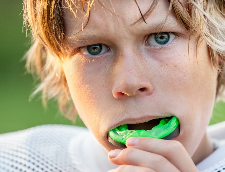 Young boy placing a green athletic mouthguard in his mouth