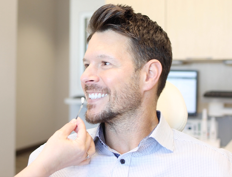 Dentist holding a veneer in front of a patient's smile