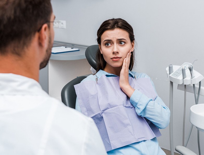 Concerned woman holding cheek while looking at emergency dentist