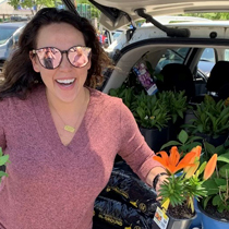 Doctor Velasco smiling in front of open car trunk filled with potted plants
