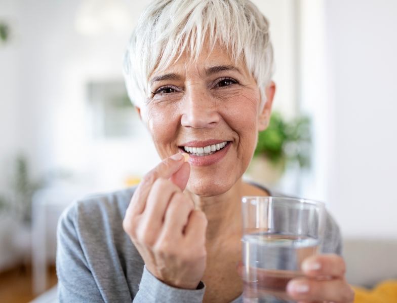 Senior woman holding pill and glass of water