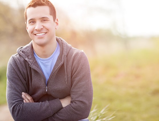 Man in grey hoodie smiling with arms folded